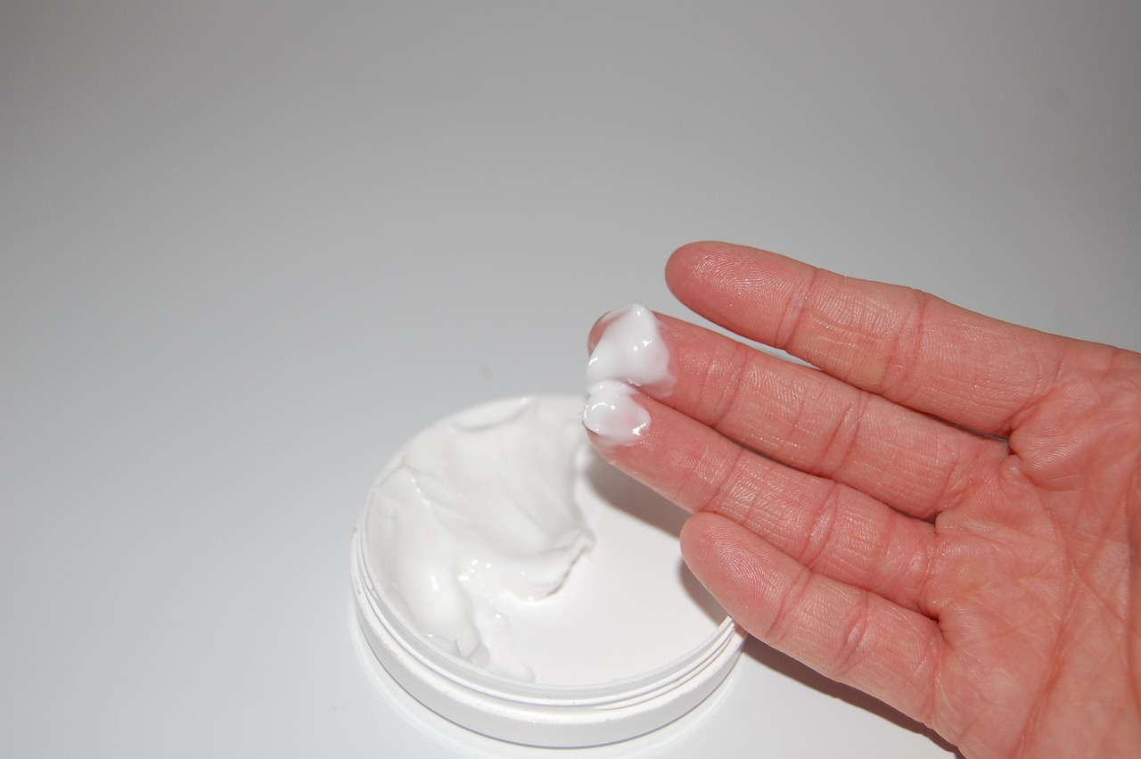 Fingertips holding a small amount of white cream above an open jar