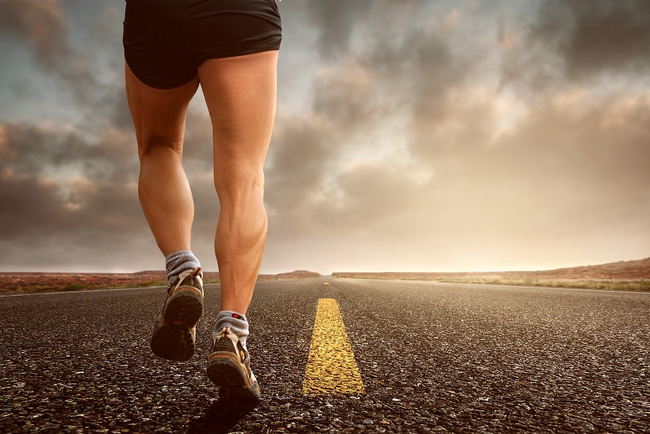 A runner in shorts and sneakers mid-stride on an open road under a cloudy sky